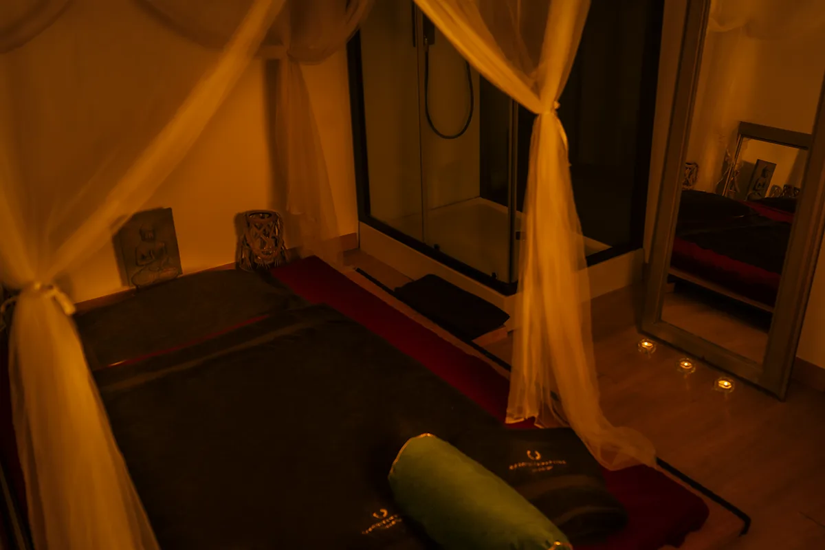 Futón bajo un dosel de tul blanco junto a la ducha y un espejo con velas, sala de masajes eróticos Zaragoza