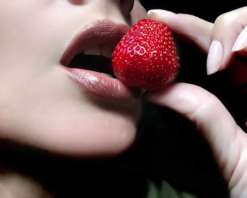 Painted lips biting a strawberry held by pale-nailed fingers, jacuzzi massage menu in Zaragoza