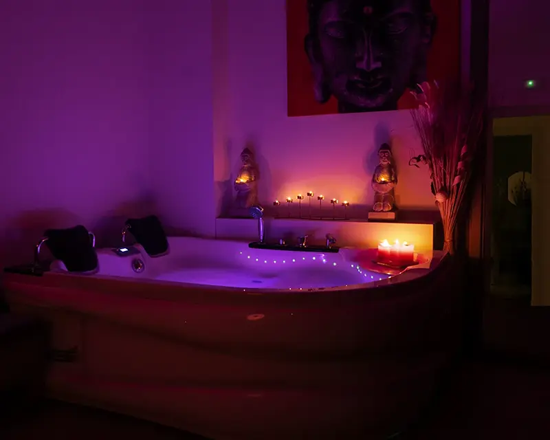 Jacuzzi bajo luz violeta con velas encendidas y un gran cuadro de Buda, masaje con jacuzzi en Zaragoza