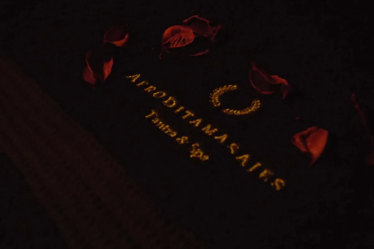 Toalla negra con el logotipo de Afrodita bordado en dorado entre pétalos de rosa, masaje sensitivo domicilio reserva Zaragoza