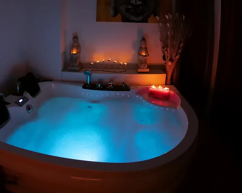Sala en penumbra con un jacuzzi de esquina lleno y con luz azul, masaje sensual mujer en Zaragoza