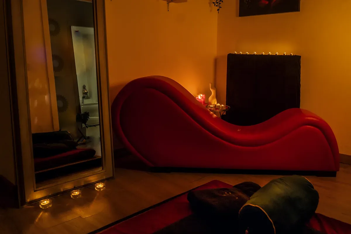 Sala en penumbra con un sofá rojo ondulado, un espejo y velas encendidas, masaje tántrico tailandés en Zaragoza