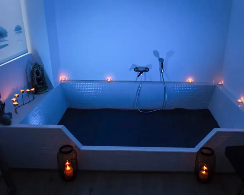 Una bañera grande enlosada con mosaico blanco bajo luz azul, masajes con ducha erótica agua Zaragoza