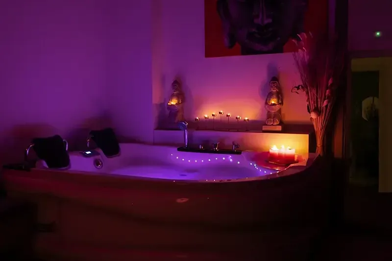 Un jacuzzi de esquina iluminado en morado con dos reposacabezas negros, masajes con ducha erótica en Zaragoza