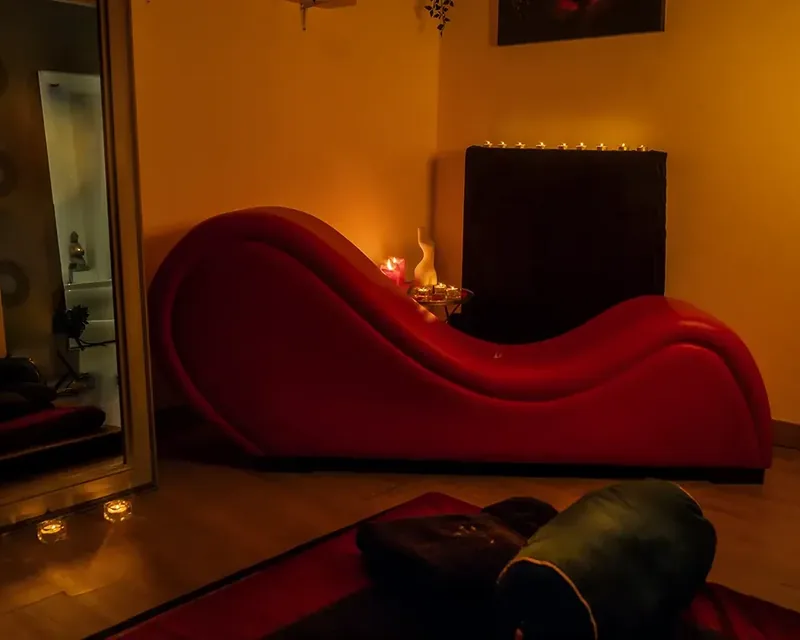 Diván tántrico rojo de forma ondulada en una sala con luz cálida, masajista erótica española diván Zaragoza