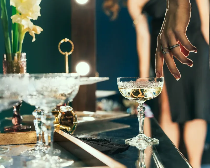 Ringed hand taking a glass of cava from a mirrored bar, VIP massage menu in Zaragoza